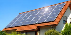 Solar panel on a red roof reflecting the sun and the cloudless blue sky